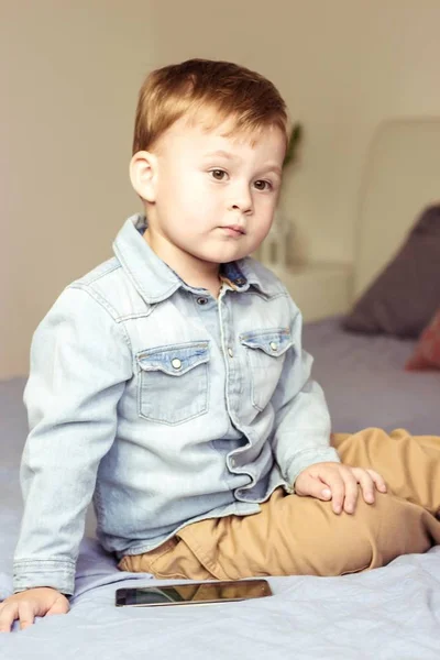 Schattig jongetje speelt op het bed. Jongen 3 jaar zittend op het bed. Gelukkig jongetje. Getinte foto. — Stockfoto