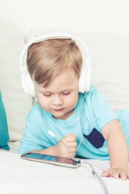 3 yıl yaşlı erkek çocuk koltukta oturur ve müzik dinliyor. Telefonda çizgi film izlerken küçük şirin çocuk. Küçük çocuk.