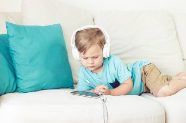 3 yıl yaşlı erkek çocuk koltukta oturur ve müzik dinliyor. Telefonda çizgi film izlerken küçük şirin çocuk. Küçük çocuk.