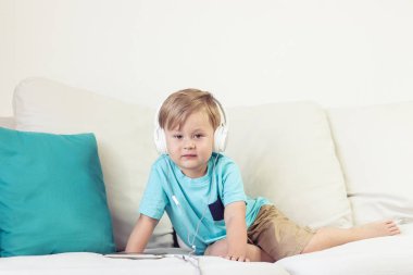 3 yıl yaşlı erkek çocuk koltukta oturur ve müzik dinliyor. Telefonda çizgi film izlerken küçük şirin çocuk. Küçük çocuk.
