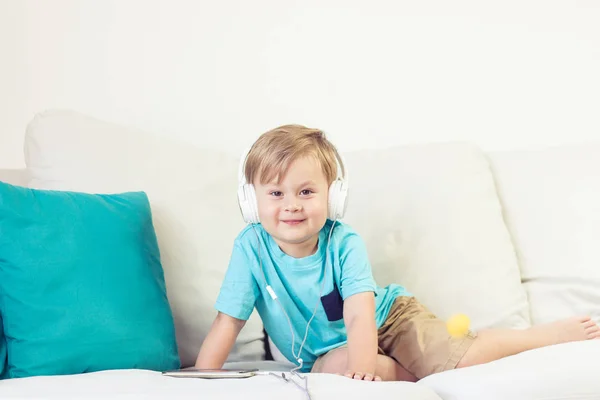 3 yıl yaşlı erkek çocuk koltukta oturur ve müzik dinliyor. Telefonda çizgi film izlerken küçük şirin çocuk. Küçük çocuk.