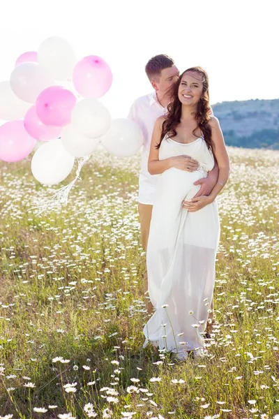 Retrato de una familia en el campo de manzanilla. Mujer embarazada sostiene cuentas. Familia con globos . — Foto de Stock