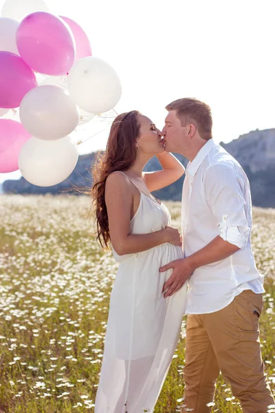 Porträtt av en familj i fältet kamomill. Gravid kvinna håller pärlor. Familj med ballonger. — Stockfoto