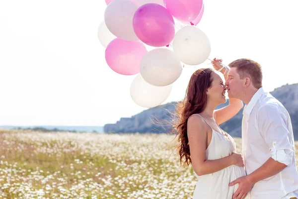 Portret van een familie op het gebied van kamille. Zwangere vrouw houdt kralen. Familie met ballonnen. — Stockfoto