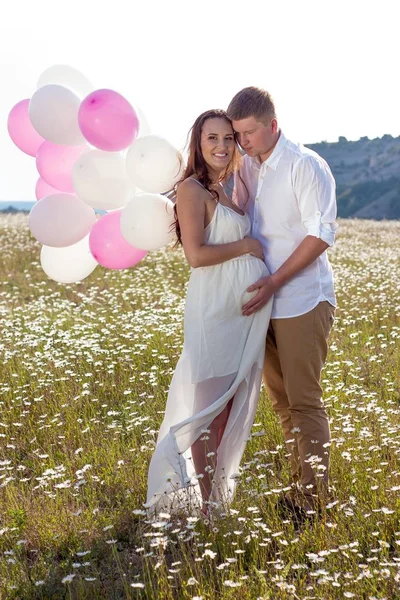 Porträtt av en familj i fältet kamomill. Gravid kvinna håller pärlor. Familj med ballonger. — Stockfoto