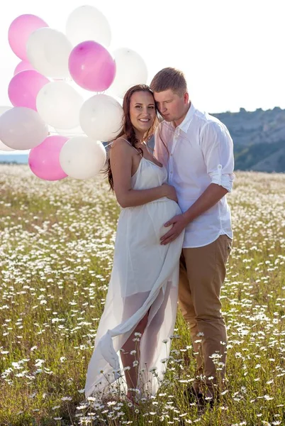 Portrait of a family in the chamomile field. Pregnant woman holds beads. Family with balloons. — Stock Photo, Image