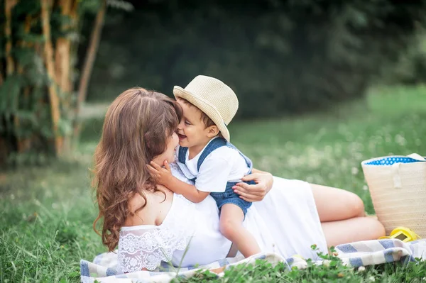 Anne ve genç oğlu çimenlerin üzerinde oynadı. Mutlu aile parkta yürüyor. Meyve yeme anne ve genç oğlu. Piknik. Yaz.