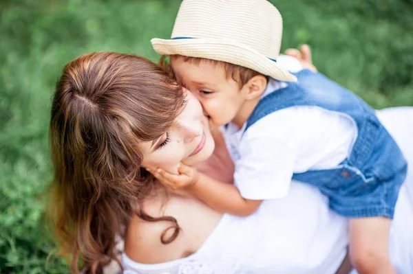 Anne ve genç oğlu çimenlerin üzerinde oynadı. Mutlu aile parkta yürüyor. Meyve yeme anne ve genç oğlu. Piknik. Yaz.