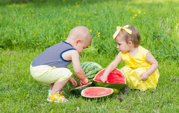 Ładny mały chłopiec i dziewczynka siedzi na trawie. Chłopiec i dziewczynka jedzenie arbuza. Letnich. Owoce. — Zdjęcie stockowe