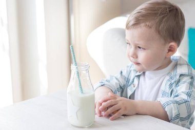 Sevimli küçük bir çocuk şeker yemek ve süt içme. Sağlık. Mutlu bir çocuk. Kahvaltı. Küçük bir oğlan masada oturuyor.