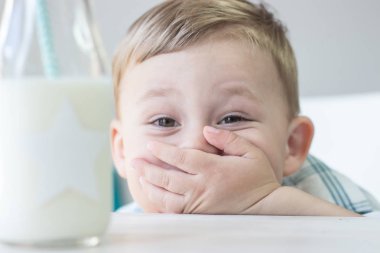 Sevimli küçük bir çocuk şeker yemek ve süt içme. Sağlık. Mutlu bir çocuk. Kahvaltı. Küçük bir oğlan masada oturuyor.