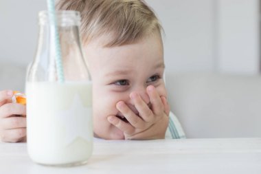 Sevimli küçük bir çocuk şeker yemek ve süt içme. Sağlık. Mutlu bir çocuk. Kahvaltı. Küçük bir oğlan masada oturuyor.