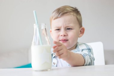 Sevimli küçük bir çocuk şeker yemek ve süt içme. Sağlık. Mutlu bir çocuk. Kahvaltı. Küçük bir oğlan masada oturuyor.