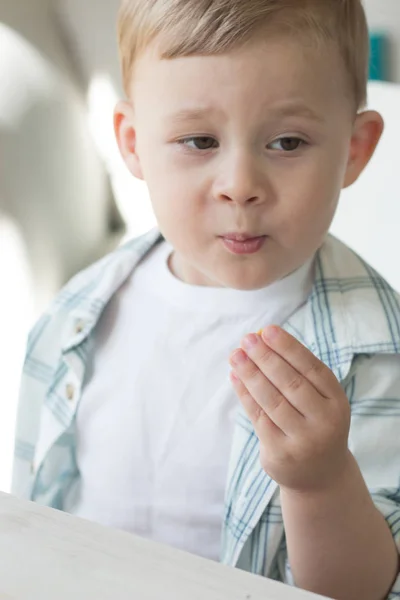 Um menino bonito está comendo doces e bebendo leite. Saúde. Criança feliz. Pequeno-almoço. Um rapazinho está sentado à mesa . — Fotografia de Stock