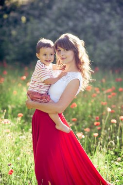 Güzel bir aile haşhaş alanına yürüyor. Küçük oğlu olan genç bir anne yürüyor. Yaz. Bahar.