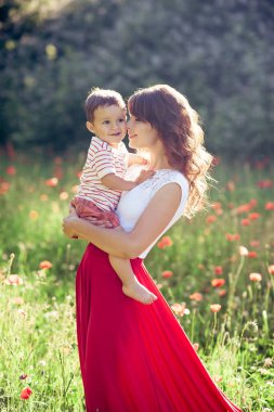 Güzel bir aile haşhaş alanına yürüyor. Küçük oğlu olan genç bir anne yürüyor. Yaz. Bahar.