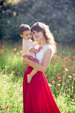 Güzel bir aile haşhaş alanına yürüyor. Küçük oğlu olan genç bir anne yürüyor. Yaz. Bahar.