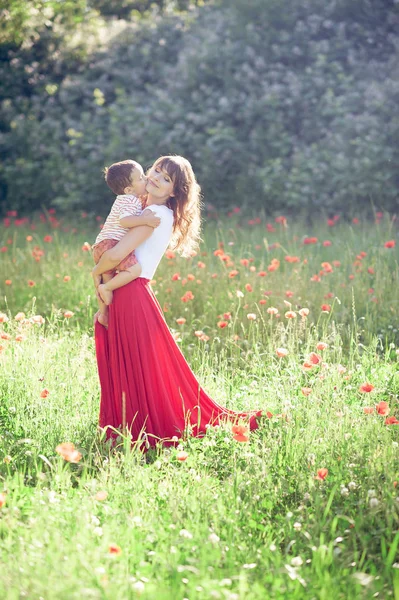 Eine schöne Familie geht in einem Mohnfeld spazieren. Eine junge Mutter mit kleinem Sohn geht. Sommer. Frühling. — Stockfoto