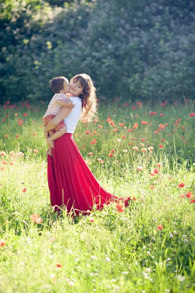 Una bella famiglia cammina in un campo di papaveri. Una giovane madre con un figlio piccolo sta camminando. Estate. Primavera . — Foto Stock