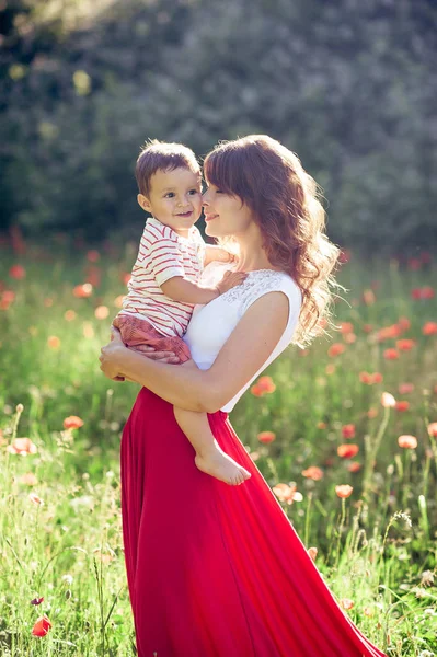Güzel bir aile haşhaş alanına yürüyor. Küçük oğlu olan genç bir anne yürüyor. Yaz. Bahar.