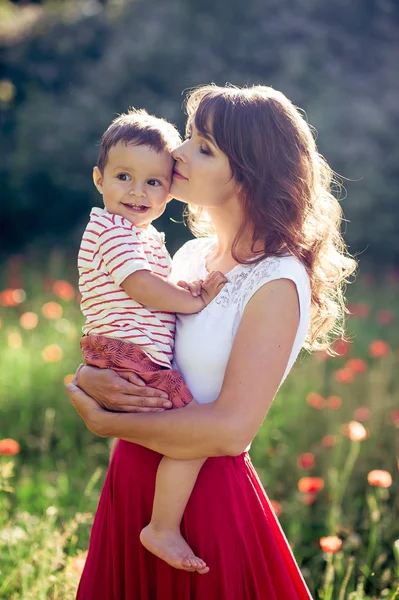 Güzel bir aile haşhaş alanına yürüyor. Küçük oğlu olan genç bir anne yürüyor. Yaz. Bahar.