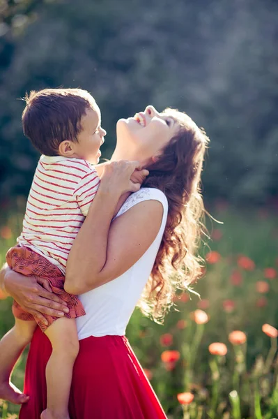 Güzel bir aile haşhaş alanına yürüyor. Küçük oğlu olan genç bir anne yürüyor. Yaz. Bahar.
