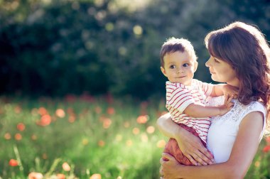Güzel bir aile haşhaş alanına yürüyor. Küçük oğlu olan genç bir anne yürüyor. Yaz. Bahar.