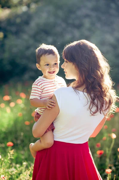 Güzel bir aile haşhaş alanına yürüyor. Küçük oğlu olan genç bir anne yürüyor. Yaz. Bahar.