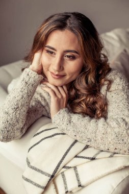 Güzel bir genç kadın rahat bir portresi. Güzel Türk kızı. Sıcak sonbahar. Rahat ev akşam. Genç bir kadın kendini bir battaniyeye sarılmış ve kanepede oturuyor.