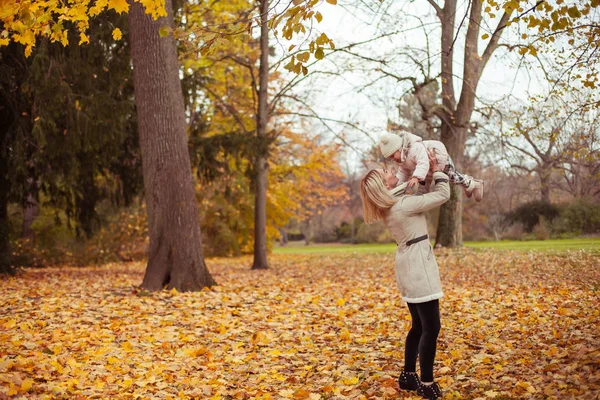 Madre joven e hija pequeña caminan en el otoño. Mamá y su hija juegan. Invierno cálido. Otoño brillante . — Foto de Stock