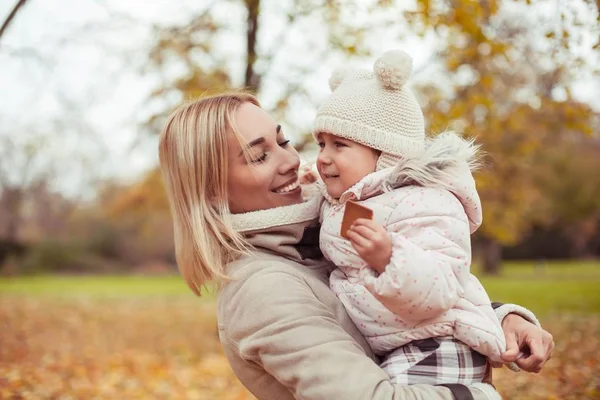 Jovem mãe e filha caminham no outono. Mãe e filha brincam. Inverno quente. Outono brilhante . — Fotografia de Stock