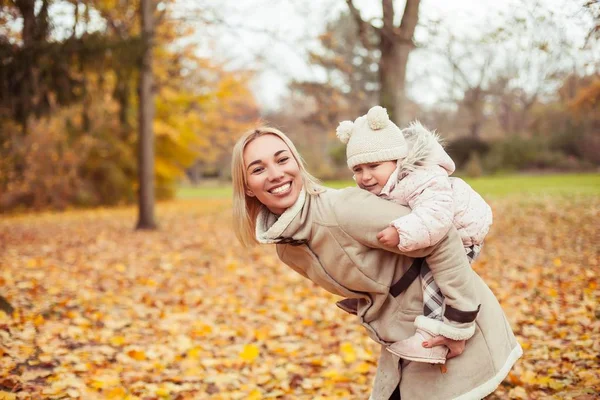 Young mother and little daughter walk in the autumn. Mom and daughter play. Warm winter. Bright autumn. — Stock Photo, Image