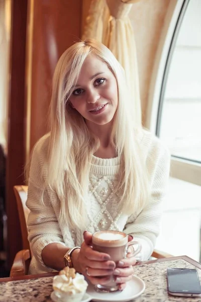 Las manos femeninas sostienen una taza de cacao caliente. Una joven está sentada en un acogedor café. La chica está bebiendo cacao. El invierno. Acogedor otoño . — Foto de Stock