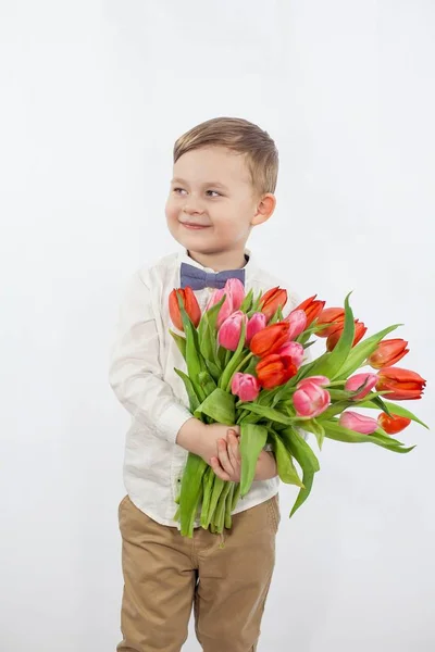 Söt liten pojke håller en bukett blommor. Tulpaner. Mors dag. Internationella kvinnodagen. Porträtt av en glad liten pojke på — Stockfoto