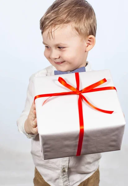 Söt liten pojke med en gåva. Lycklig pojke håller en box med en gåva. Mors dag. Internationella kvinnodagen. Porträtt av en glad liten pojke på en vit bakgrund. Våren. Födelsedag. — Stockfoto