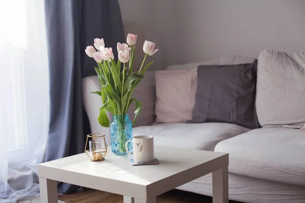 Innenraum. Ein Strauß Tulpen in einer Glasvase, heißer Tee, ein Kerzenständer auf einem Couchtisch. Zimmer. Gemütlich. Sofa. — Stockfoto