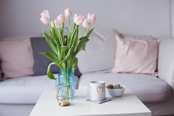 Interiør. En buket tulipaner i en glas vase, varm te, en lysestage på et sofabord. Værelse. Hyggeligt. Sovesofa . - Stock-foto