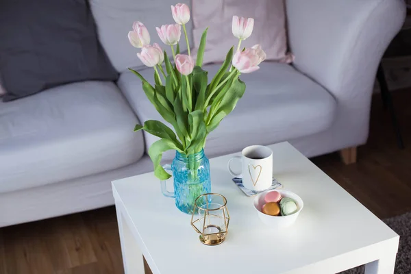 Interior. A bouquet of tulips in a glass vase, hot tea, a candle stand on a coffee table. Room. Cozy. Sofa. — Stock Photo, Image