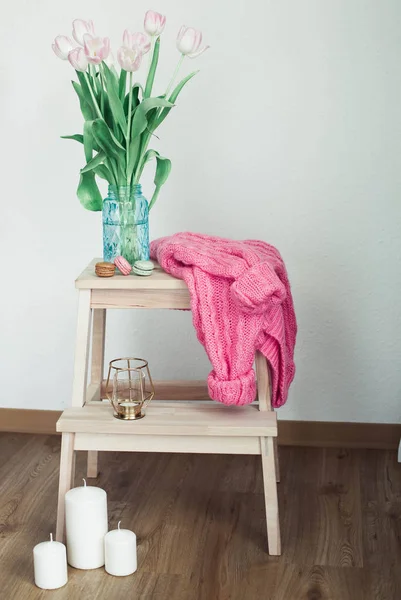 Home decoration. Cozy decor. A bouquet with tulips, a beautiful knitted sweater, a candle stand on a wooden pedestal. Spring. Birthday, holidays, mother's day. International Women's Day.