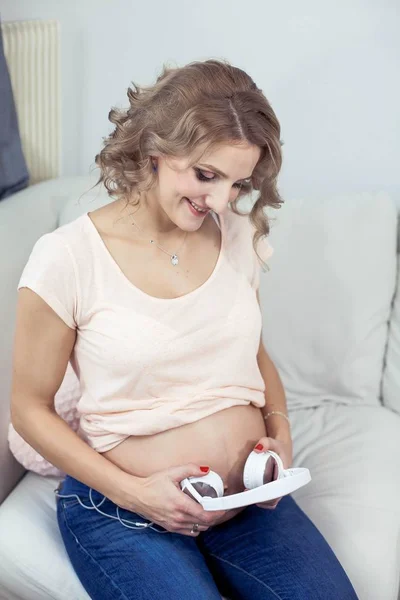 Молода красива вагітна жінка відпочиває вдома. Молода вагітна жінка слухає музику. Портрет красивої вагітної жінки. Жінка тримає навушники . — стокове фото
