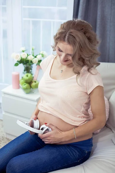 Молодая красивая беременная женщина отдыхает дома. Молодая беременная женщина слушает музыку. Портрет красивой беременной женщины. Женщина держит наушники . — стоковое фото