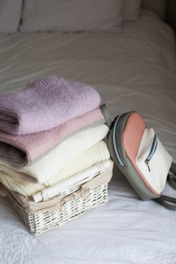 Bir sepet yatakta temiz şeylerle. Rahat. Kazak örme, sırt çantası. Bahar kıyafetleri.
