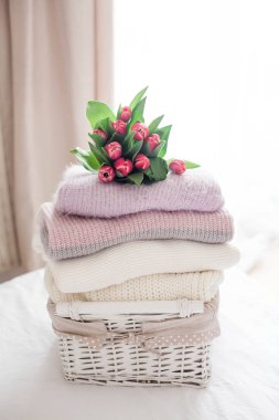 Bir sepet yatakta temiz şeylerle. Rahat. Örme kazak, Lale buketi. Bahar kıyafetleri.