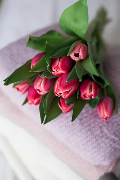 Ein Korb mit sauberen Sachen auf dem Bett. Gemütlich. Strickpullover, Tulpenstrauß. Frühlingskleidung. — Stockfoto