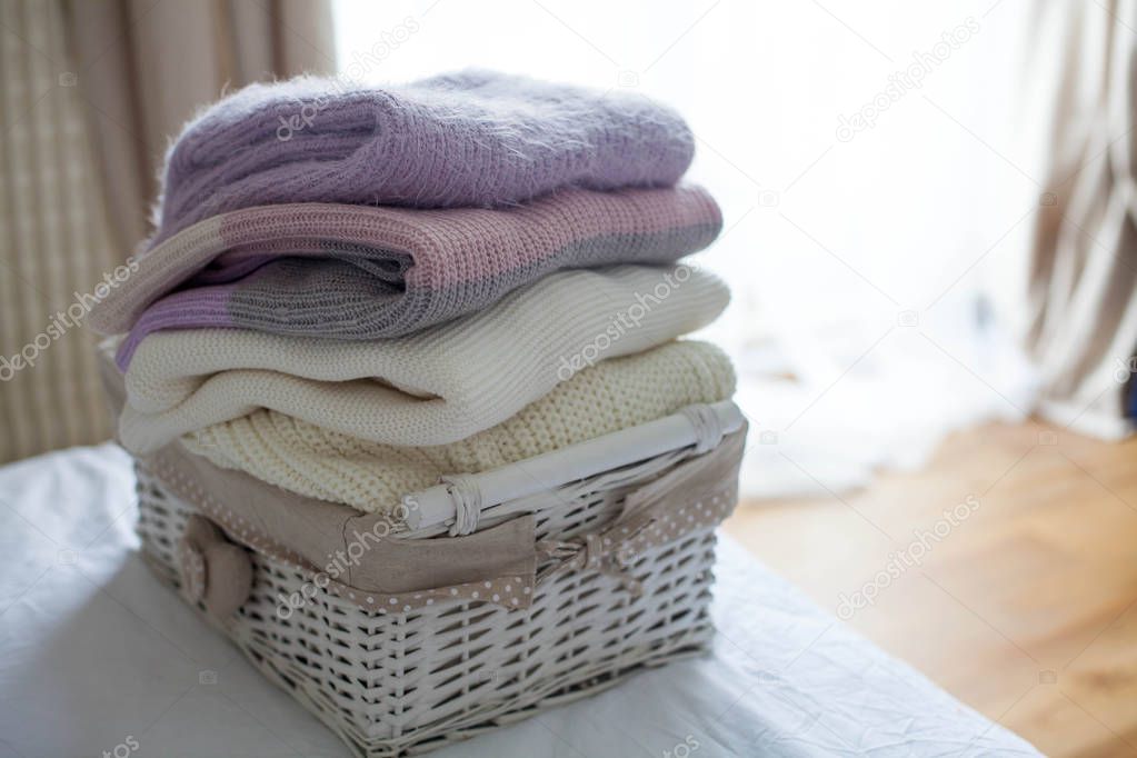 A basket with clean things on the bed. Cozy. Knitted sweaters.