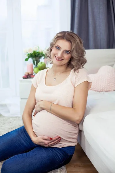 Νέοι όμορφη έγκυος γυναίκα ξεκουράζονται στο σπίτι. Άνετο. Μια νεαρή γυναίκα στέκεται δίπλα στο παράθυρο. Εγκυμοσύνη. Η μητρότητα. — Φωτογραφία Αρχείου