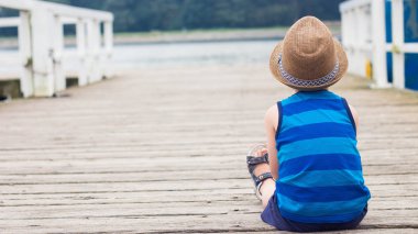 Sevimli küçük bir çocuk iskelede oturuyordu. Sahilde mutlu küçük çocuk. Yaz. Rekreasyon. Turizm. Deniz.