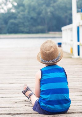 Sevimli küçük bir çocuk iskelede oturuyordu. Sahilde mutlu küçük çocuk. Yaz. Rekreasyon. Turizm. Deniz.