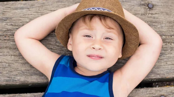 En söt liten pojke ligger på piren. Glad liten pojke på stranden. Sommaren. Rekreation. Turism. Havet. — Stockfoto