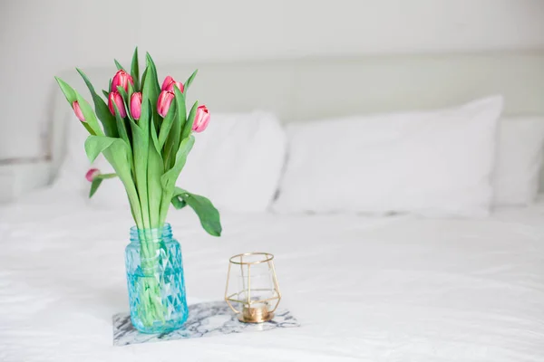 Home interior. Bedroom. A bouquet of tulips in a glass vase, a candle, a tray, a box with a gift stand on the bed. Morning. Spring. Summer. Holidays. International Womens Day. Mothers Day. — Stock Photo, Image